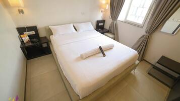 A hotel room with a bed, bedside tables, a lamp, and a window with curtains.