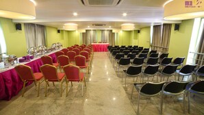 Una sala de conferències amb files de cadires, una barra de bufet i un escenari amb estovat vermell.