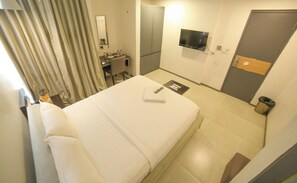 A hotel room with a bed, a desk, a mirror, a TV, and a wardrobe. - M3 Boutique Hotel (Madurai)