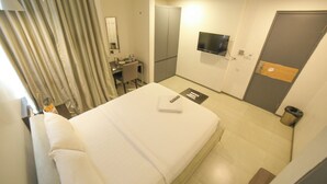 Habitació d'hotel amb llit, escriptori, mirall, televisió i armari.