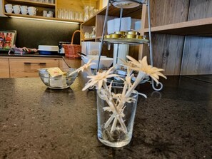 A kitchen counter with a glass vase containing dried flowers, a metal tray with a tea set, and a wooden shelf with cups and jars. - Haus Bergheim (Sankt Leonhard im Pitztal)