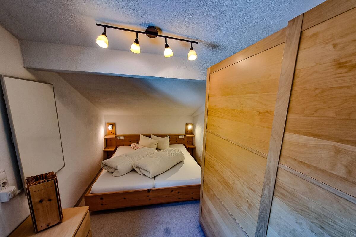 A small, cozy bedroom with a wooden bed, a nightstand, a mirror, and a ceiling light fixture.