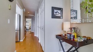 A hallway with a wooden floor, a refrigerator, a dining area with a table and chairs, and a wall-mounted cabinet with a lamp. - 3rd fl. Bayfront condo, balcony, parking, bikes (San Diego)
