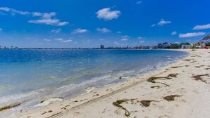 A beach with clear blue water, sandy shore, and buildings in the background. - 3rd fl. Bayfront condo, balcony, parking, bikes (San Diego)