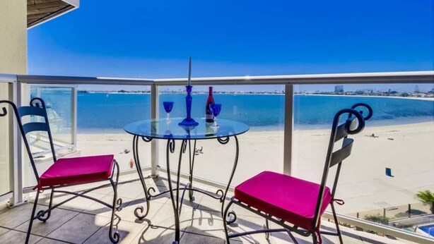 A balcony with a glass table and chairs, overlooking a beach. - 3rd fl. Bayfront condo, balcony, parking, bikes (San Diego)
