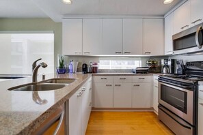 A modern kitchen with a granite countertop, stainless steel sink, and a built-in oven. - 3rd fl. Bayfront condo, balcony, parking, bikes (San Diego)