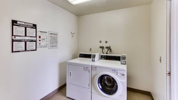 A laundry room with two washing machines and dryers, a ceiling light, and informational signs on the wall. - 3rd fl. Bayfront condo, balcony, parking, bikes (San Diego)