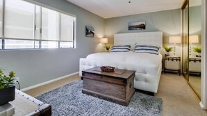 A bedroom with a large bed, a bedside table, a mirror, and a window. - 3rd fl. Bayfront condo, balcony, parking, bikes (San Diego)