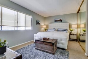 A bedroom with a large bed, a bedside table, a mirror, and a window. - 3rd fl. Bayfront condo, balcony, parking, bikes (San Diego)