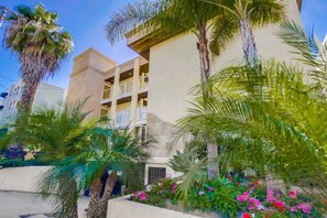 A multi-story hotel with balconies, surrounded by palm trees and flowering plants. - 3rd fl. Bayfront condo, balcony, parking, bikes (San Diego)