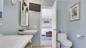 A bathroom with a white sink, mirror, and toilet. There is a television mounted on the wall and a framed picture on the wall. - 3rd fl. Bayfront condo, balcony, parking, bikes (San Diego)