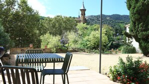 Une terrasse avec une table et des chaises, entourée de verdure et offrant une vue lointaine sur une tour.