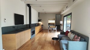 Une cuisine moderne avec des armoires en bois, un comptoir noir et un four encastré. On y trouve un coin repas avec une table et des chaises, ainsi qu’un canapé avec des coussins.