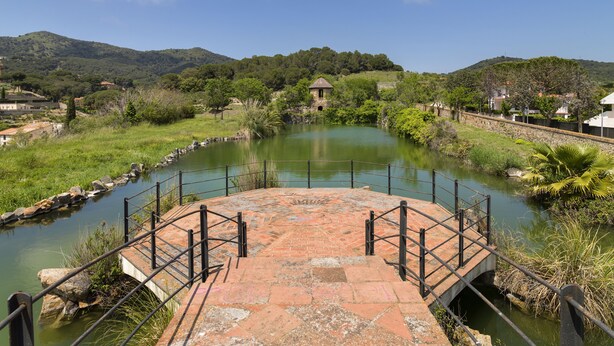 Un pont de pierre enjambe une rivière paisible, et on aperçoit au loin un petit kiosque, entouré de verdure et de collines.