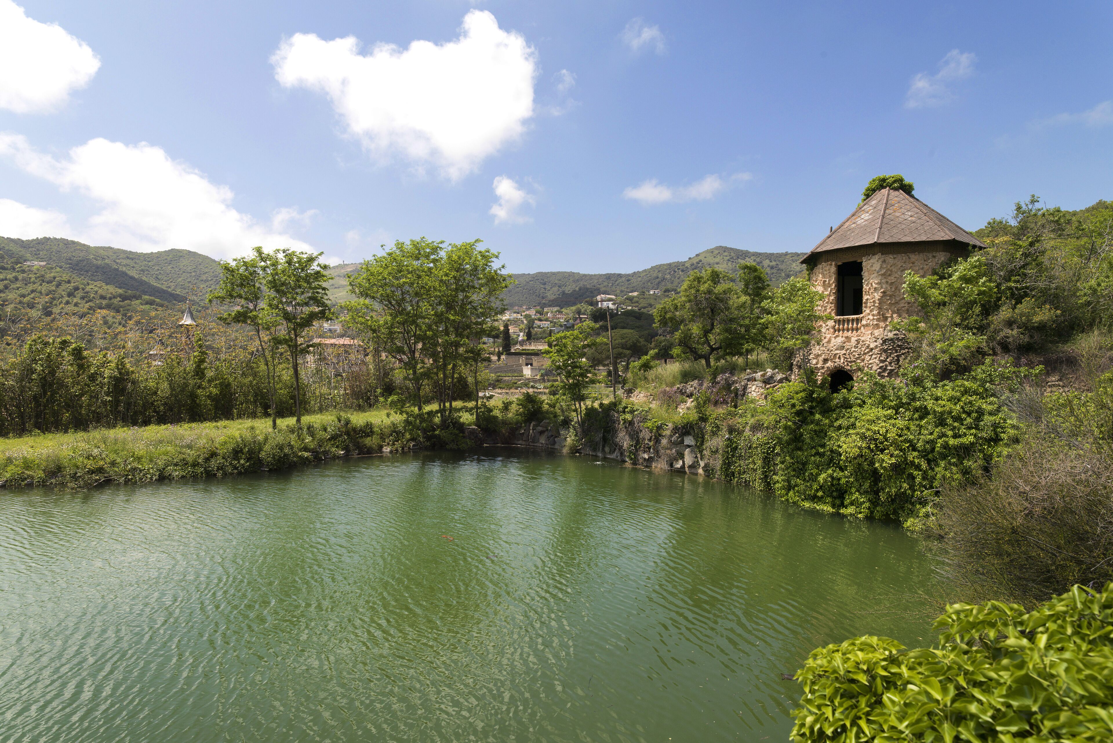 A stone tower with a conical roof overlooking a calm river, surrounded by lush greenery and hills.