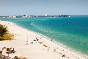 Una playa con vista despejada al océano, una orilla arenosa y algunos edificios a lo lejos.