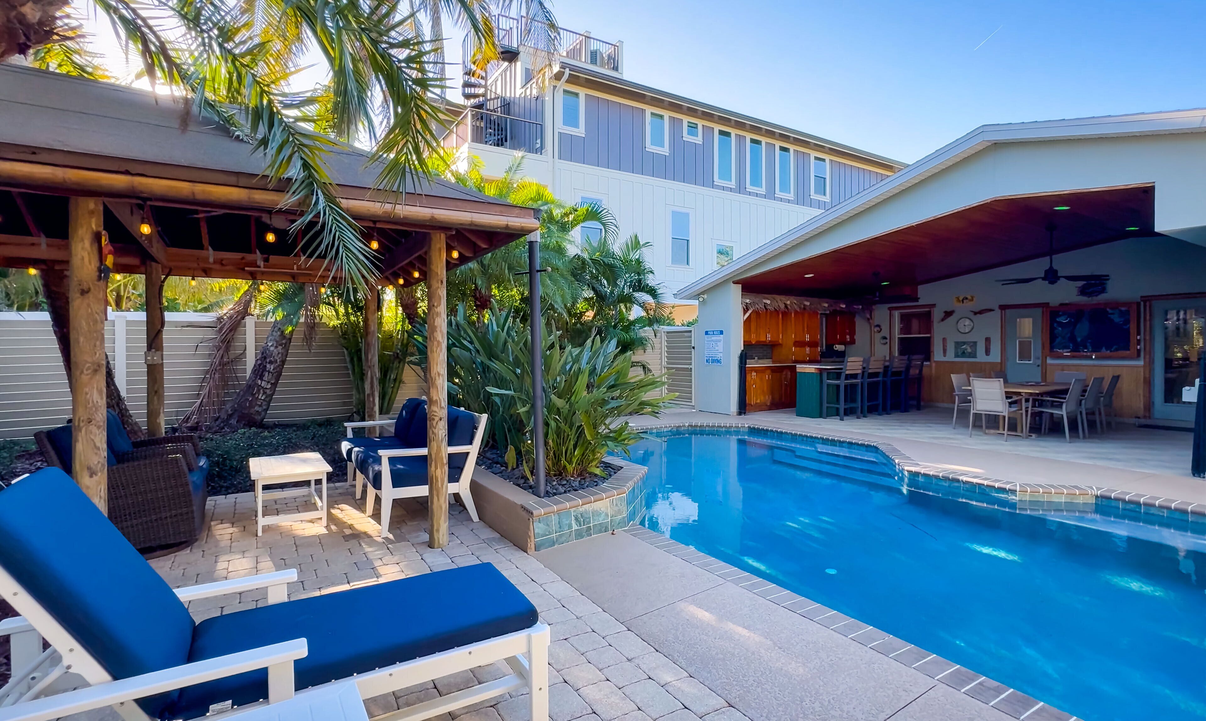 Ein Garten mit Swimmingpool, Sitzgelegenheiten im Freien und einer überdachten Terrasse.