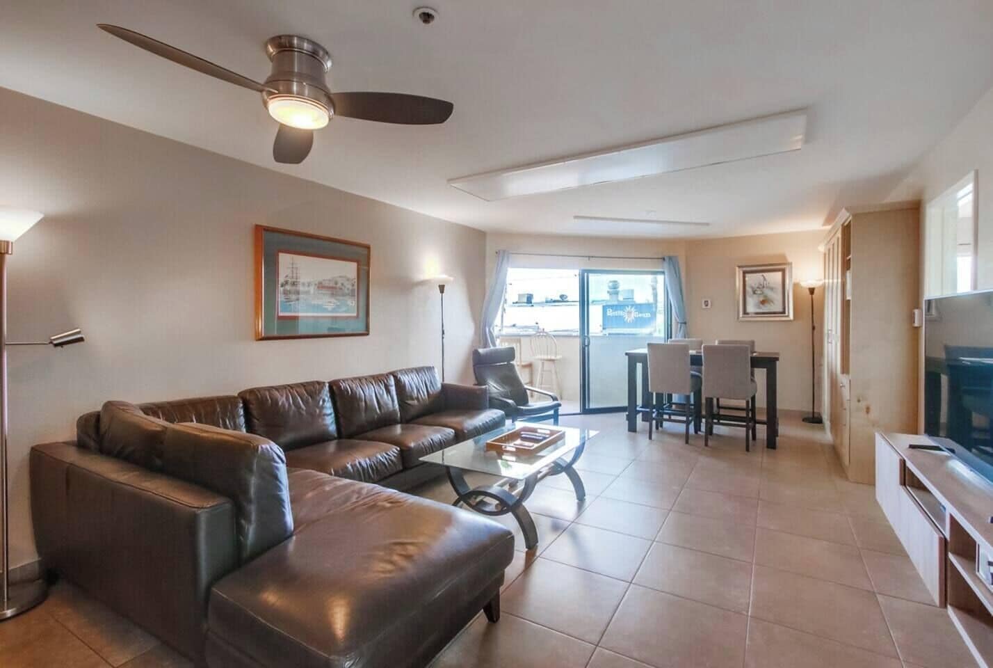 A living room with a leather sofa, a coffee table, a television, and a ceiling fan.
