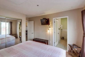 Ein Hotelzimmer mit Bett, einer Sitzbank, einem an der Wand montierten Fernseher und einer Tür zu einem Badezimmer.