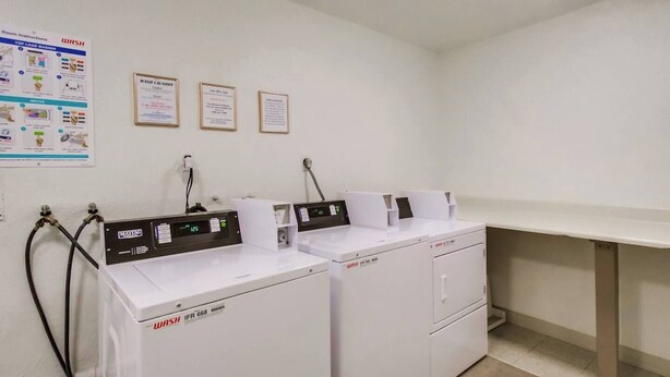 A laundry room with two white washing machines, a control panel, and a wall-mounted sign with instructions.