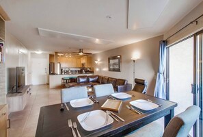 Ein modernes Wohnzimmer mit Essbereich, einer Küche im Hintergrund und einem großen Schiebeglasfenster rechts.