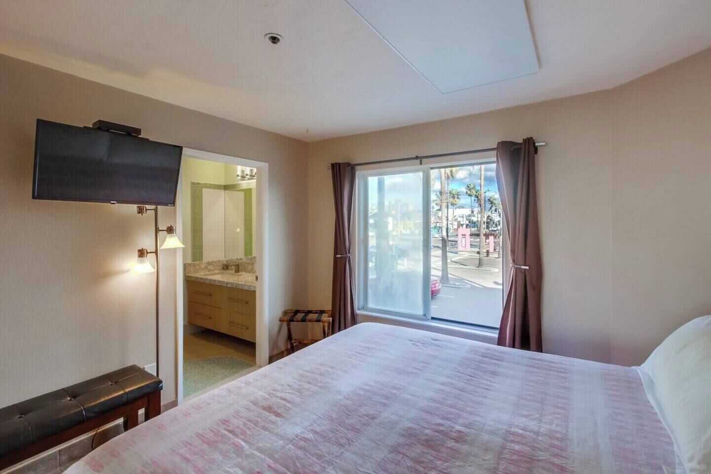 A hotel room with a bed, a television, a bathroom with a mirror, and a view of the outside.