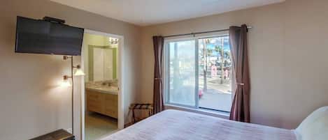 Habitación de hotel con cama, televisor, baño con espejo y vista al exterior.