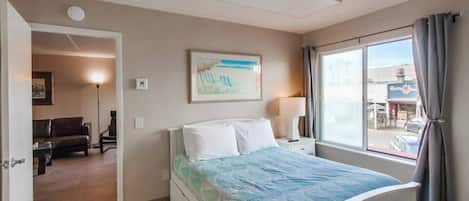 Habitación de hotel con cama, mesita de noche, lámpara, un cuadro y vistas al exterior.