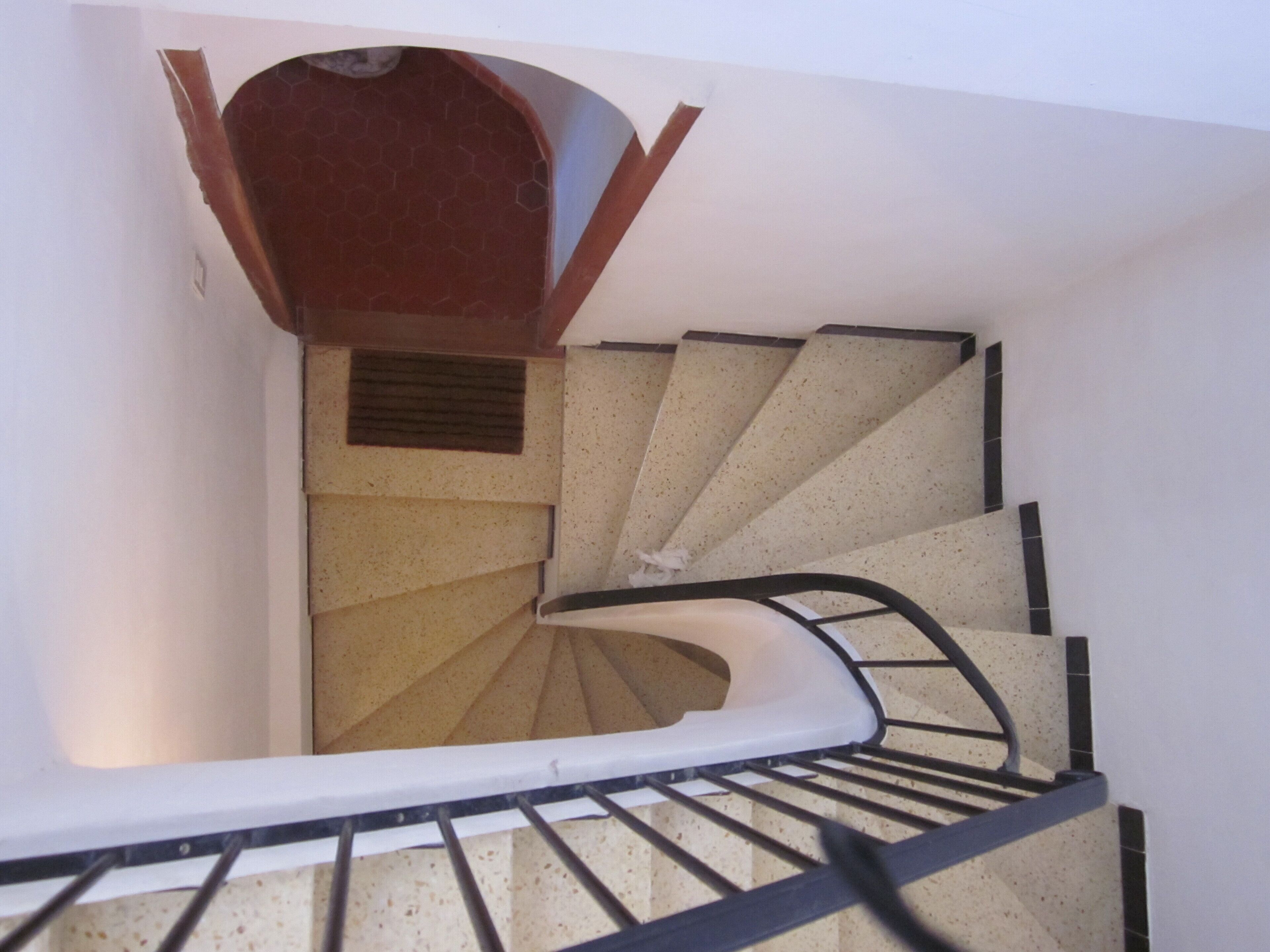 A spiral staircase with a handrail, a wooden landing, and a small window at the top.