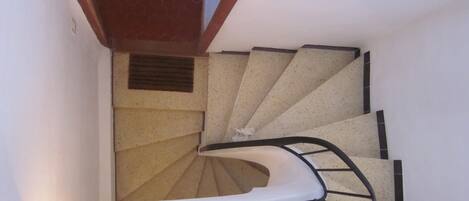 A spiral staircase with a handrail, a wooden landing, and a small window at the top.