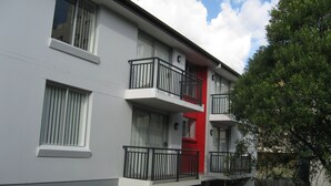 Un immeuble moderne à plusieurs étages, doté de balcons, de grandes fenêtres et d’une porte rouge.