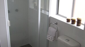 Une salle de bain avec une douche à parois de verre, des toilettes et une fenêtre sur le rebord de laquelle sont posées des bougies.