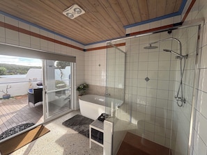 Un bagno moderno con cabina doccia in vetro, una vasca da bagno freestanding e un'uscita in vetro verso un'area esterna.