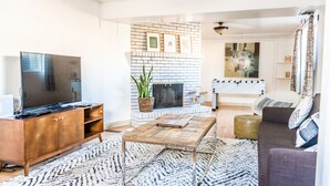A living room with a brick fireplace, a television, a coffee table, and a sofa. - Bright family friendly 3 bed 2 bath w/3 king beds located near AFA (Colorado Springs)
