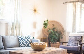 Una sala de estar acogedora con un sofá, una mesa de centro con una cesta tejida y una mesa redonda de madera.