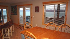 Comedor con mesa y sillas de madera, zona de cocina con barra y vista al agua a través de una ventana.