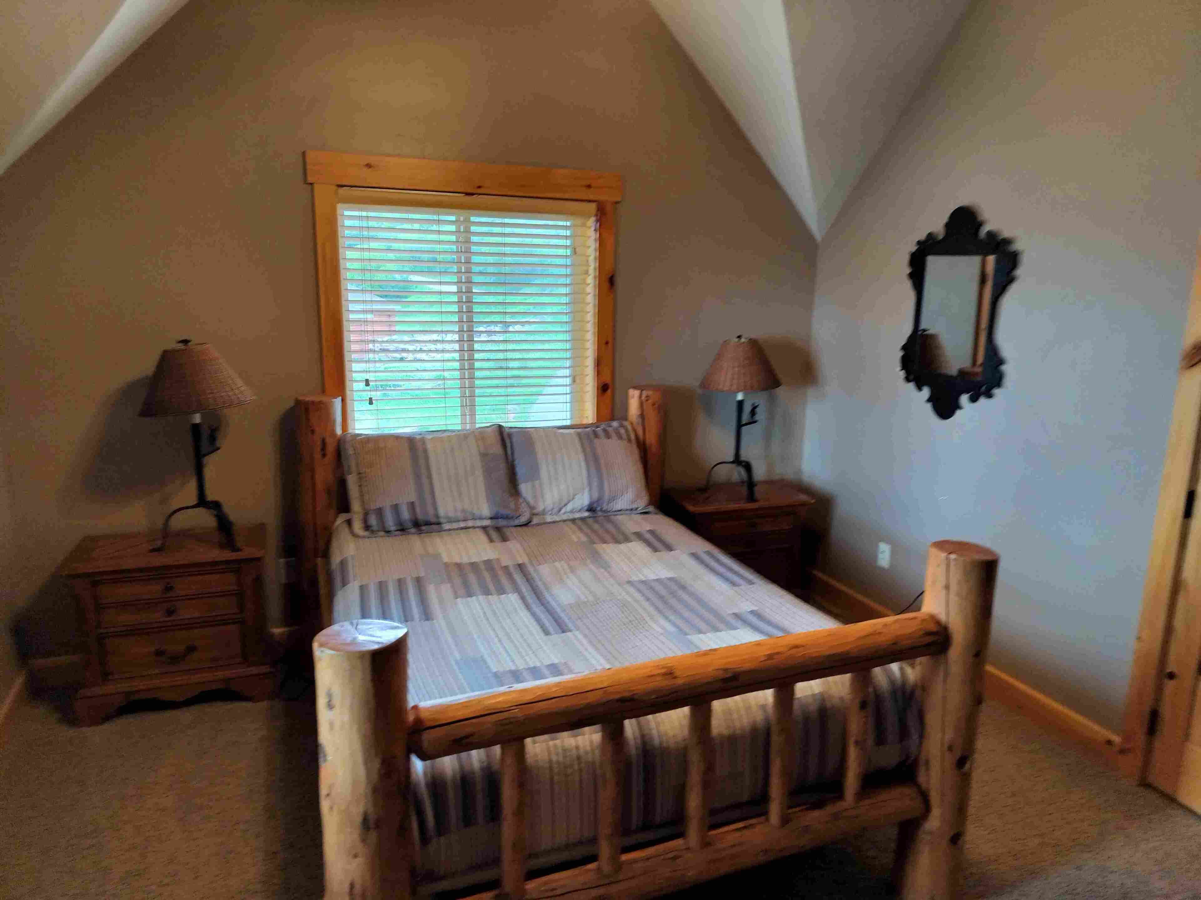 Un dormitorio con una cama de madera, dos mesitas de noche, una ventana con persianas y un espejo en la pared.