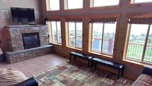 Una sala de estar con chimenea de piedra, ventanas amplias, televisor de pantalla plana y alfombra estampada.
