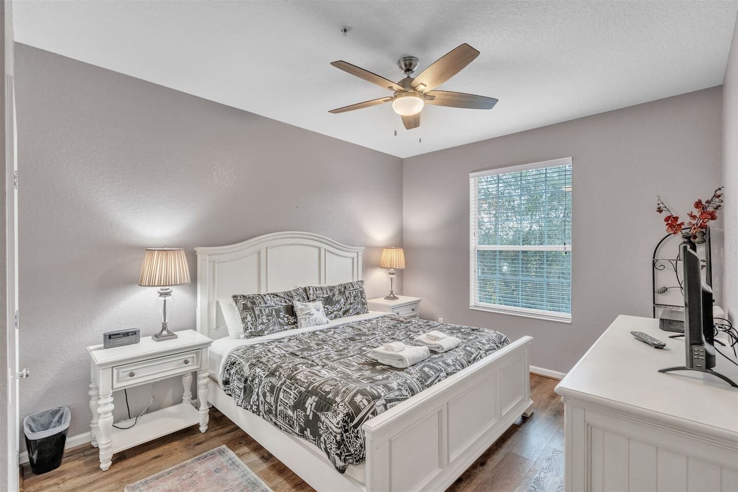 A bedroom with a bed, bedside tables, a ceiling fan, a window, and a desk with a computer.
