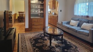 Een woonkamer met een bank, salontafel en een eethoek met stoelen en een tafel. Een keuken is zichtbaar door een open doorgang.