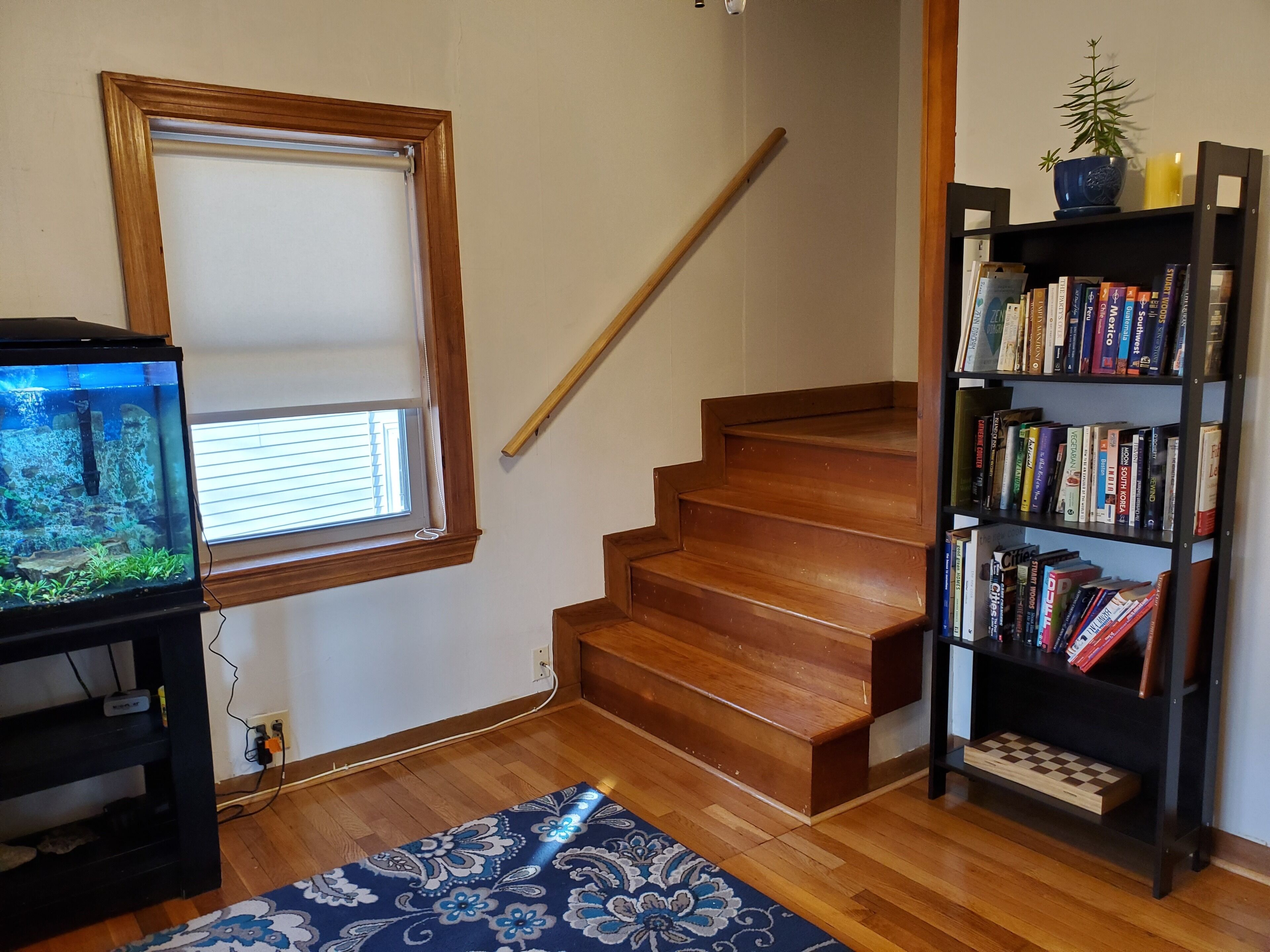 A staircase with wooden steps, a bookshelf filled with books, a fish tank, and a window with blinds.
