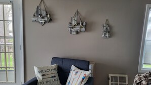 A room with a dark blue sofa, a 'Welcome to the Lake' pillow, and rustic wall decor.