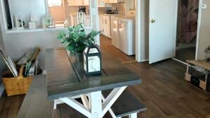 A kitchen with white cabinets, a dining table with a potted plant, and a wooden floor.