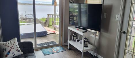 A living room with a sofa, a television on a stand, a sliding glass door leading to a deck, and a view of the water.