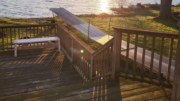 A wooden deck with a bench and a covered area overlooking a body of water during sunset.