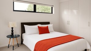 A neatly made bed with white linens and a red throw blanket, a bedside lamp, and a wardrobe with a mirror.
