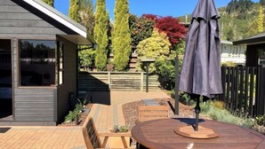A modern patio with a wooden table and chairs, a covered umbrella, and a variety of plants and trees. - “CedarView at Kinloch” - a brilliant 3 bedroom holiday home with stunning views  (Kinloch)