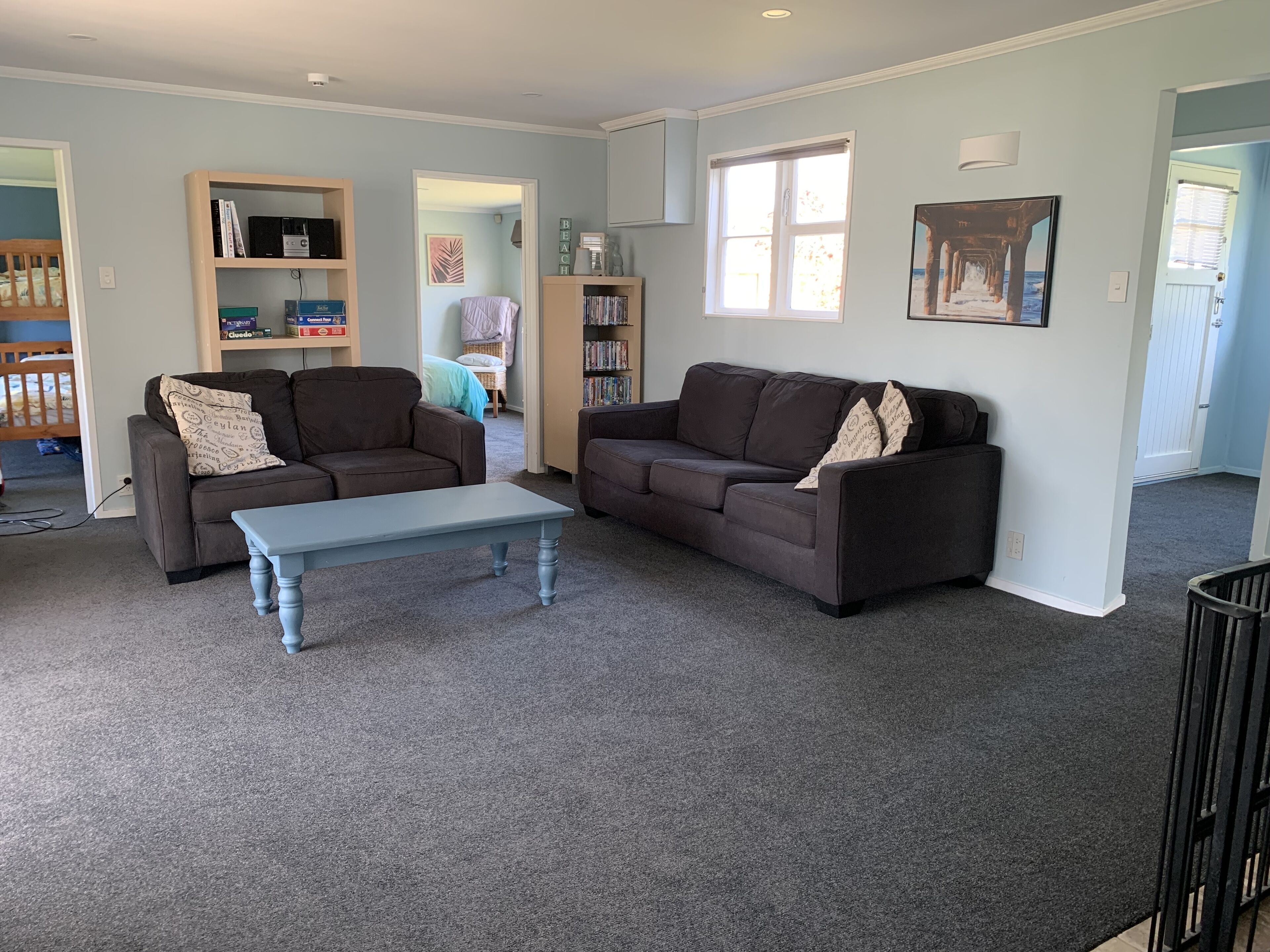 Uma sala de estar ampla com dois sofás marrom escuro, uma mesa de centro azul claro e uma estante repleta de livros e objetos decorativos.