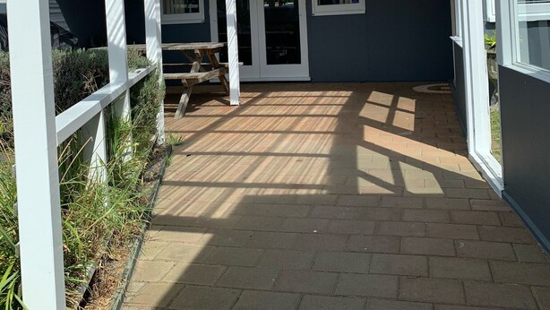 Ein überdachter Patio-Bereich mit Glasdach, einer Holzbank und einem Backsteinboden.