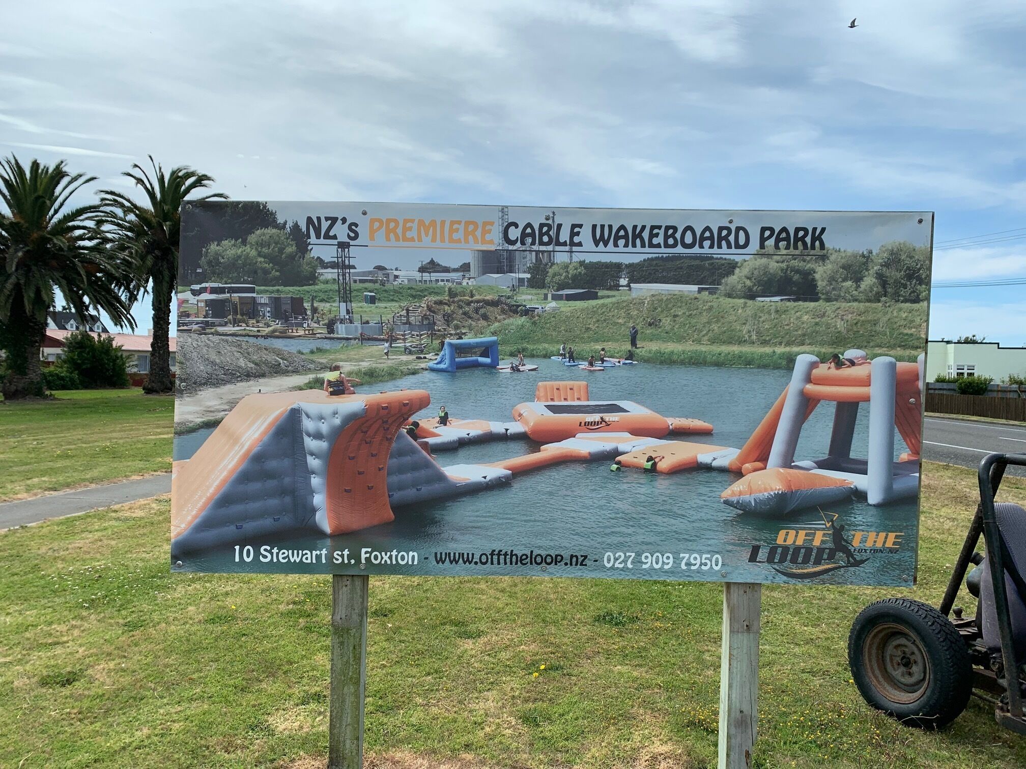Une enseigne indiquant l'emplacement du premier parc de wakeboard sur câble de Nouvelle-Zélande, avec des obstacles gonflables pour la pratique du wakeboard.
